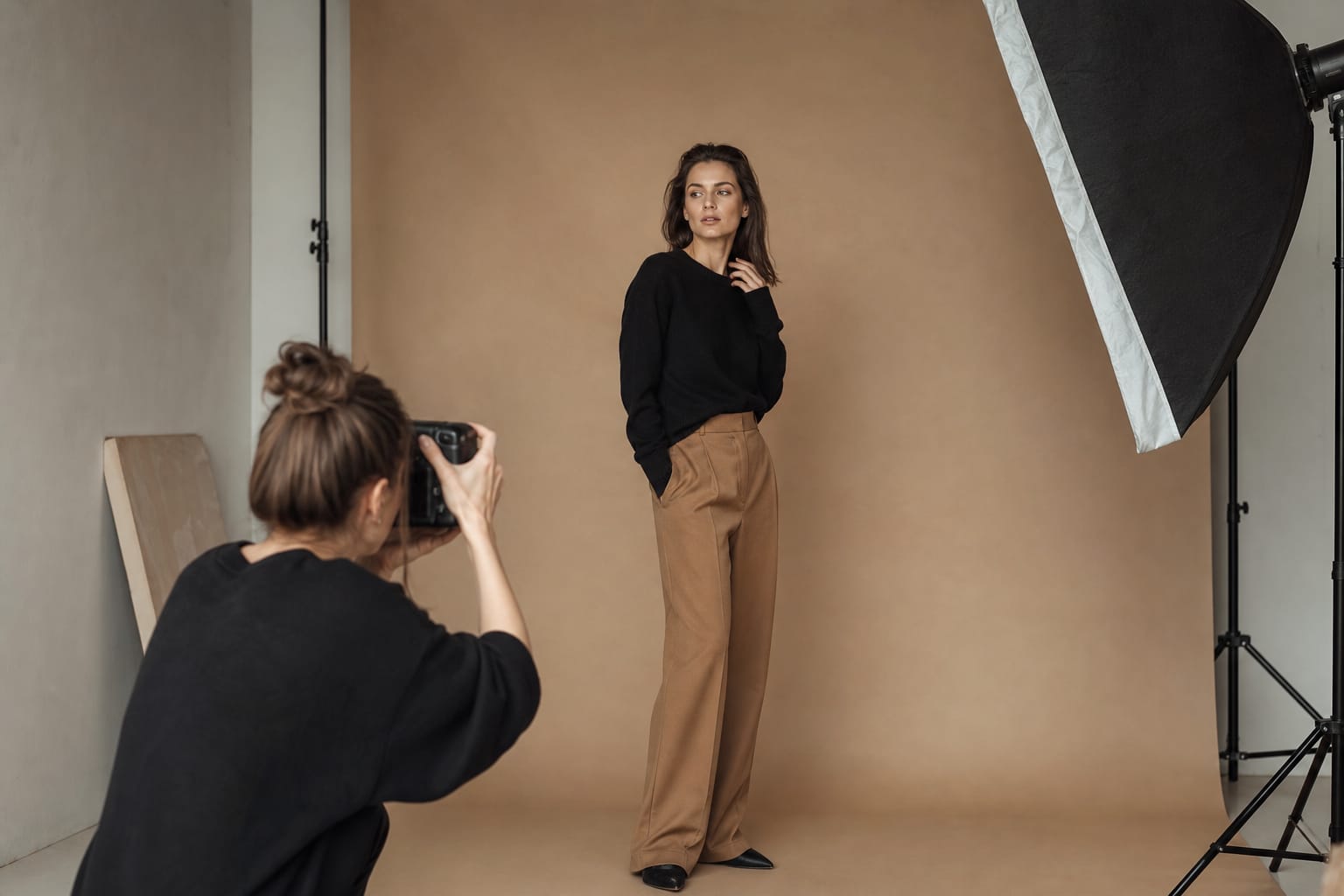 A print model at a studio shoot A print model posing for a photographer in a studio with a light stand and a warm beige backdrop